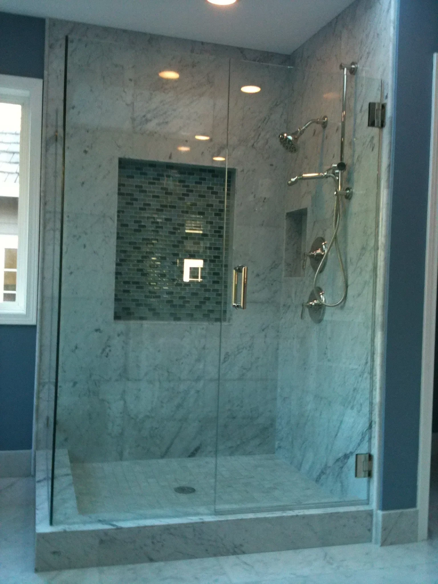 Marble walk-in shower with frameless glass and a mosaic niche