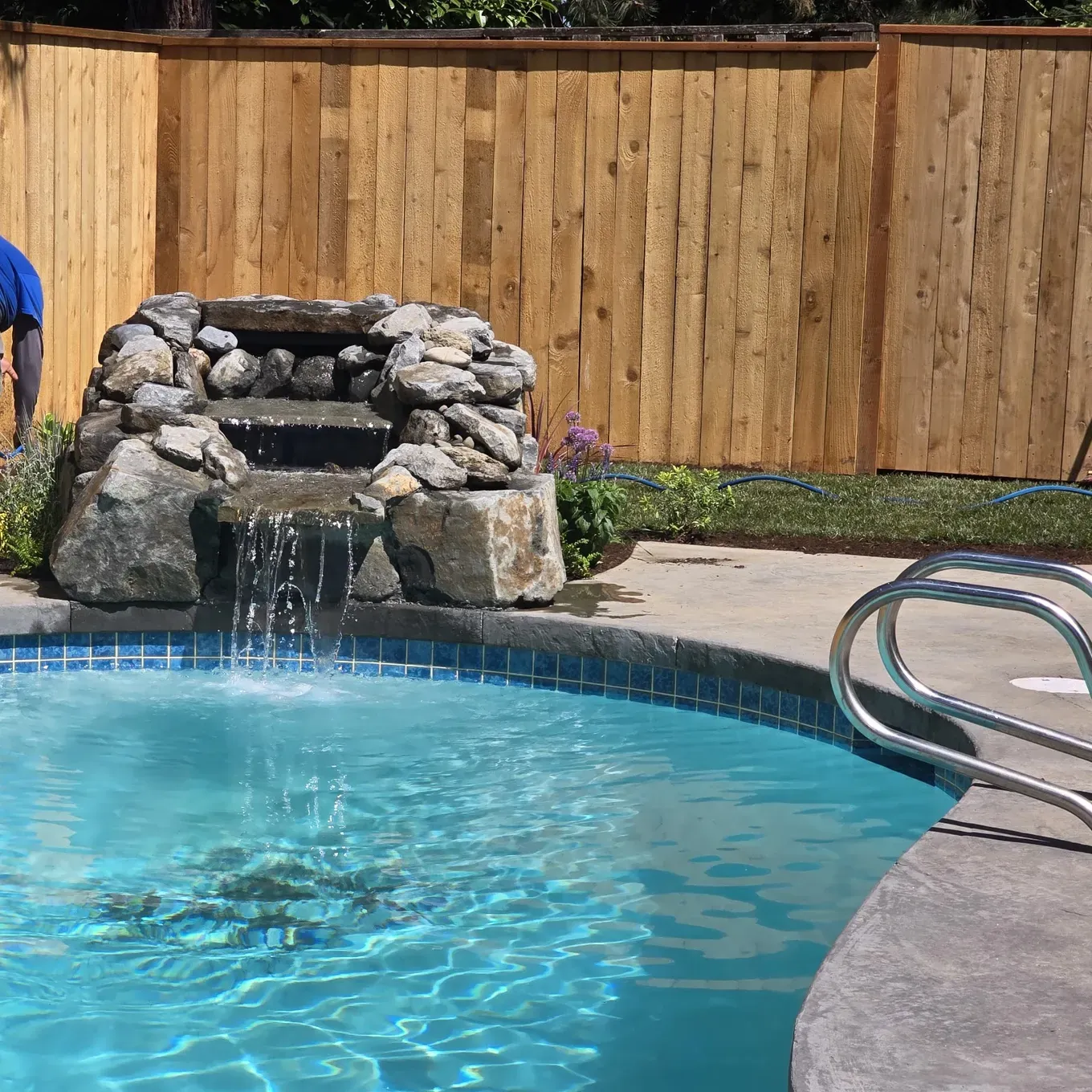 Custom stacked-rock waterfall spilling into the renovated pool over a blue tile band