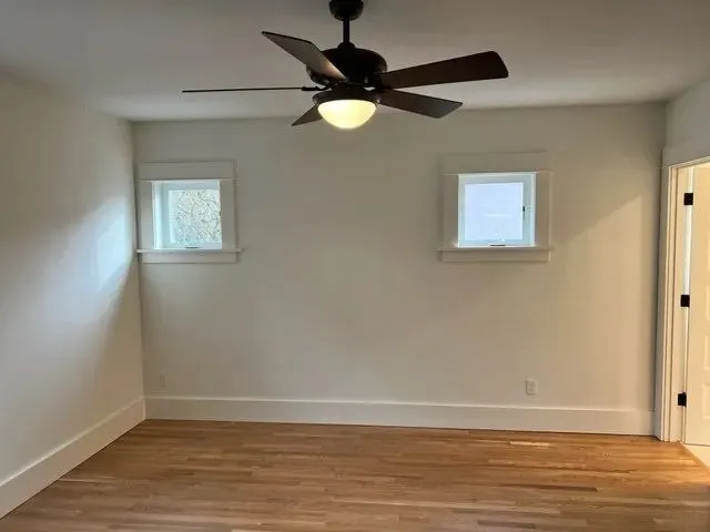 Empty bedroom with ceiling fan, two small windows, refinished oak floor