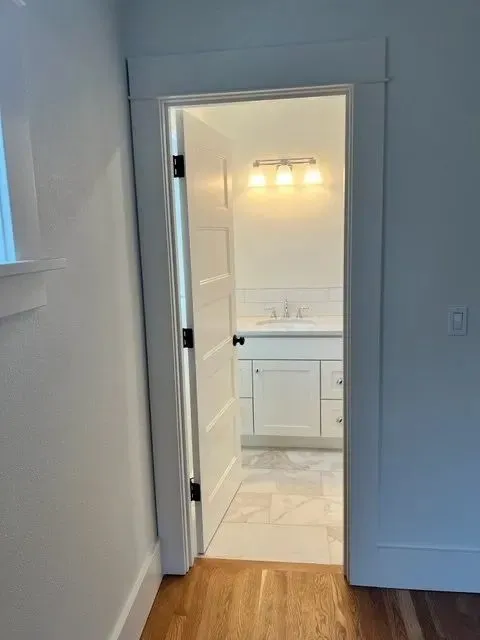 View through doorway into bath — white vanity lit by twin sconces