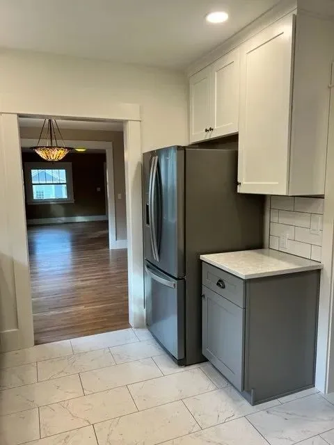 Gray and white kitchen with stainless French-door fridge and view to dining