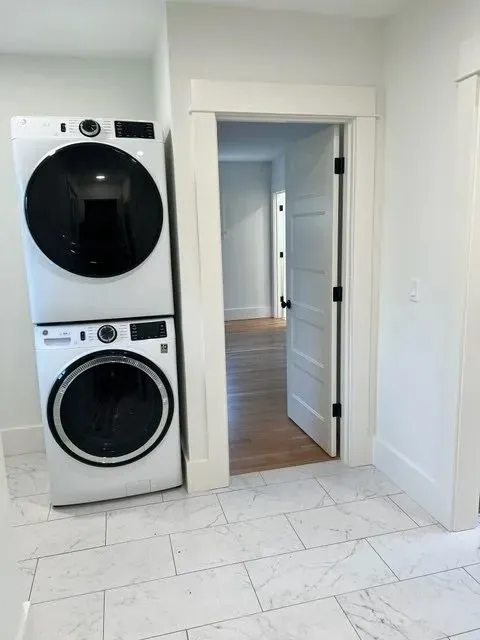 Laundry alcove with stacked white washer and dryer on marble tile