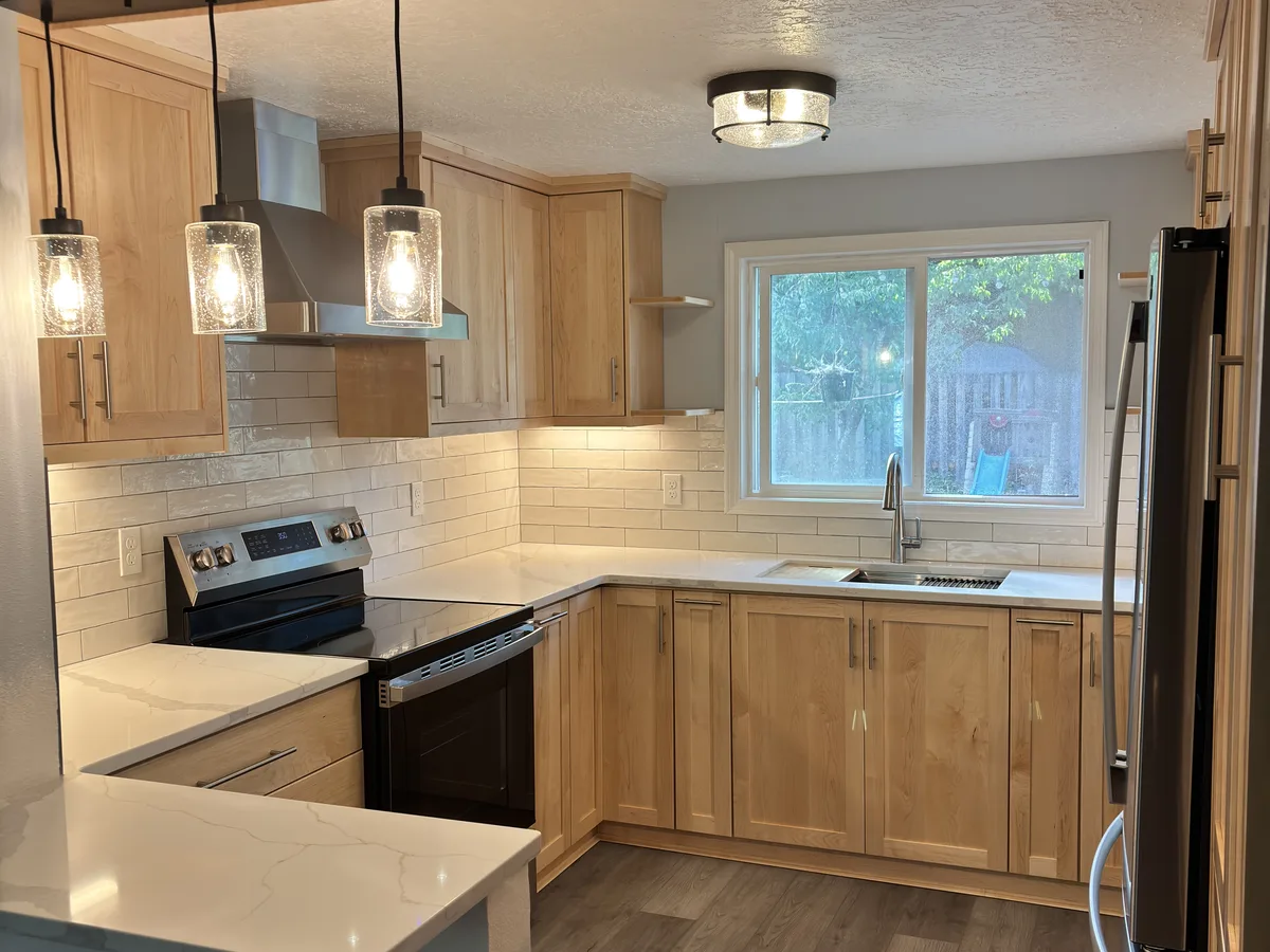 The finished kitchen with custom maple cabinets, quartz counters, and seeded glass pendants