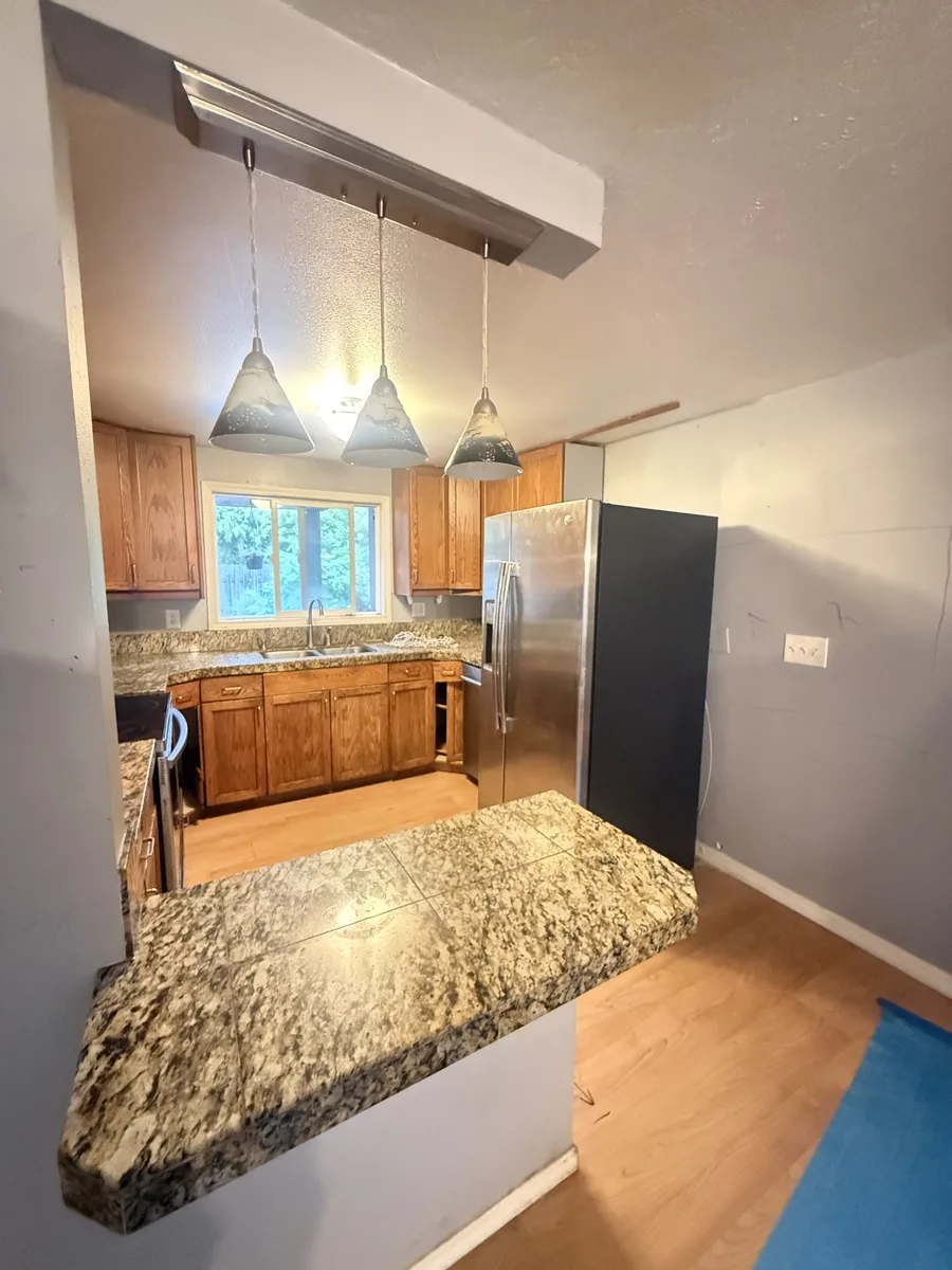 Old kitchen sink wall with oak cabinets, three pendants, and a stainless refrigerator