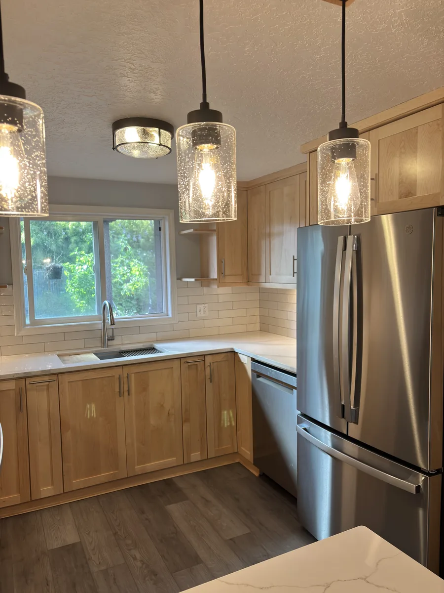 Finished sink wall with maple cabinets, white tile, seeded glass pendants, and a stainless refrigerator