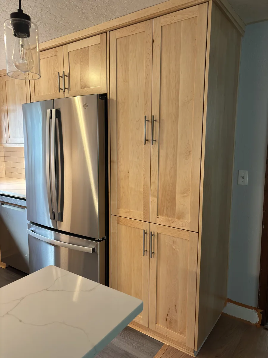 Stainless refrigerator beside a full height maple pantry cabinet