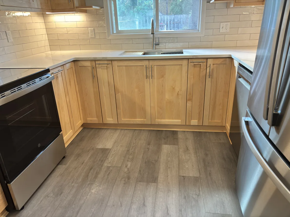 Maple base cabinets, quartz counter, and grey plank flooring under the window