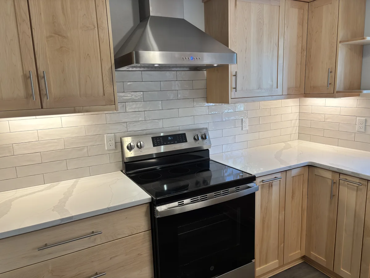 Range wall with a stainless chimney hood over white tile and quartz