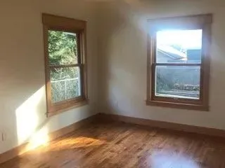 Empty room with refinished hardwood and original wood-trim windows